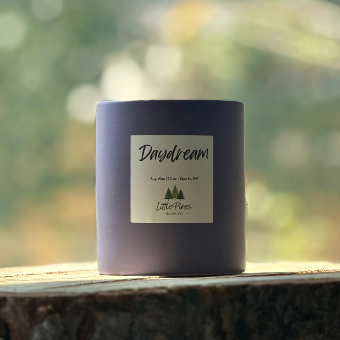Purple candle labeled 'Daydream' by Little Pines on a wooden surface with a blurred natural background