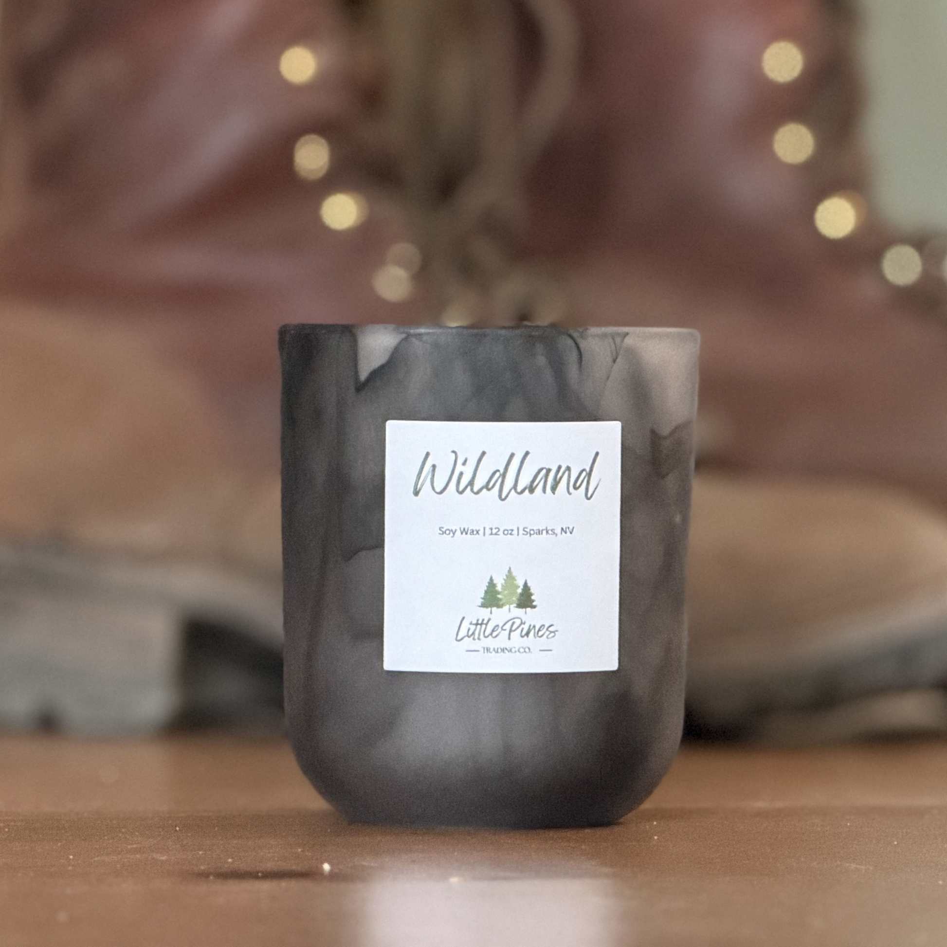 Candle with 'Wildland' label on a wooden surface, blurred lights in the background